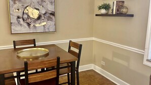 A dining area with a wooden table and chairs, a large abstract painting on the wall, and two shelves with decorative items. - FIFA 2026 Walk to Stadium | 2BR Unit 4G ATL (Atlanta)