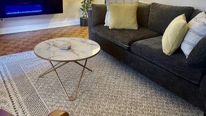 A living room with a dark grey sofa, a marble coffee table, a patterned rug, a flat-screen TV, a floor lamp, and a fireplace with a blue light. - FIFA 2026 Walk to Stadium | 2BR Unit 4G ATL (Atlanta)
