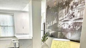 Una sala de estar moderna con piso de madera, una mesa de centro negra, un jarrón blanco y una lámpara.
