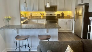 A modern kitchen with white cabinetry, a granite countertop, stainless steel appliances, and a central island with bar stools. - FIFA 2026 Walk to Stadium | 1BR Unit 24B ATL (Atlanta)