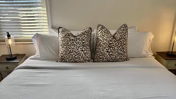 A neatly made bed with white sheets, two leopard print pillows, and a folded dark towel on the bed.