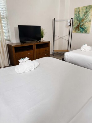 Ein Hotelzimmer mit zwei Betten, einem Fernseher auf einer Holzkommode, einem Handtuch auf jedem Bett, einer Pflanze und einem Gemälde an der Wand.