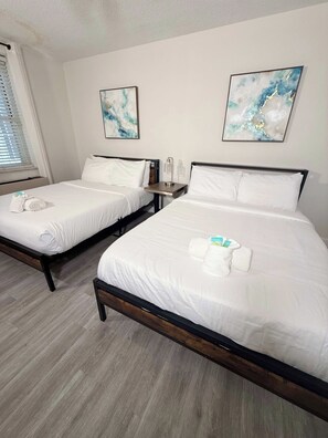 Une chambre d’hôtel avec deux lits, chacun équipé de draps et de serviettes blancs, une table de chevet avec une lampe et des œuvres d’art abstraites accrochées aux murs.