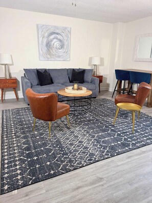 Un salon moderne avec un canapé gris, deux fauteuils, une table basse et un tapis à motifs.