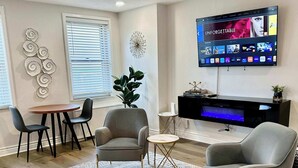 Un salon moderne doté d’un téléviseur à écran plat, de fauteuils gris, d’une table basse et d’un ventilateur de plafond.