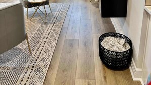Un salon moderne comprenant un canapé, des fauteuils, une table basse, un téléviseur fixé au mur et une plante décorative.