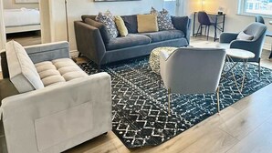 Un salon moderne avec un canapé gris, des coussins à motifs, un fauteuil blanc et un tapis noir et blanc.
