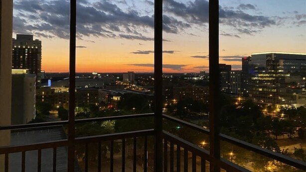 Une vue sur la ville au crépuscule, avec des bâtiments et des lumières visibles à travers la rambarde d’un balcon.
