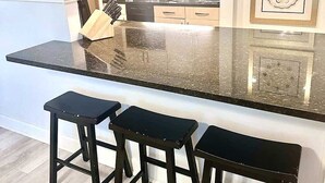 A kitchen with a black countertop, three stools, and a microwave. - FIFA 2026 Walk to Stadium | 1BR Unit 4E ATL (Atlanta)