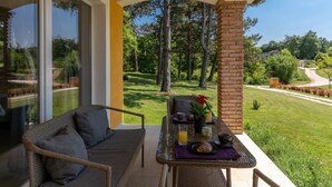 A patio with wicker furniture, a glass table, and a view of a green lawn and trees. - Villa Kristina (Istria - Pazin) (Pazin)
