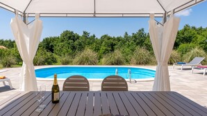 A covered outdoor seating area with a pool view, a bottle of champagne, and two glasses on a table. - Villa Kristina (Istria - Pazin) (Pazin)