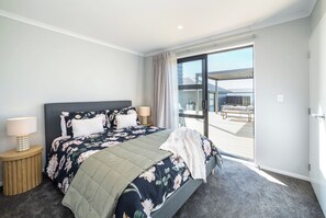 A bedroom with a bed, two bedside tables, a window, and a view of an outdoor deck. - Sunset On Syrah, Martinborough (Martinborough)