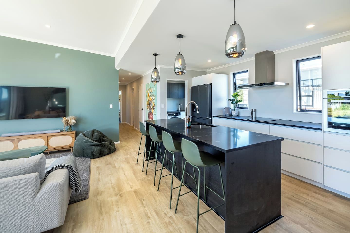 A modern kitchen with a central island, bar stools, pendant lighting, and a large window providing natural light.