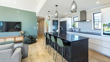 A modern kitchen with a central island, bar stools, pendant lighting, and a large window providing natural light.