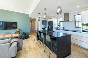 A modern kitchen with a central island, bar stools, pendant lighting, and a large window providing natural light. - Sunset On Syrah, Martinborough (Martinborough)