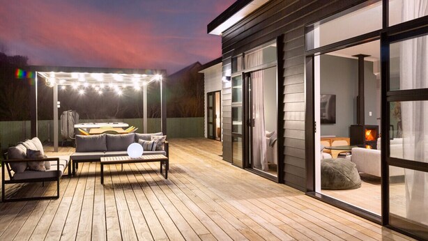 A modern outdoor deck with a hot tub, seating area, and large sliding glass doors leading to an interior living space. - Sunset On Syrah, Martinborough (Martinborough)