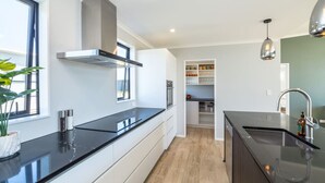 A modern kitchen with black countertops, white cabinetry, a stainless steel range hood, and a built-in oven. - Sunset On Syrah, Martinborough (Martinborough)