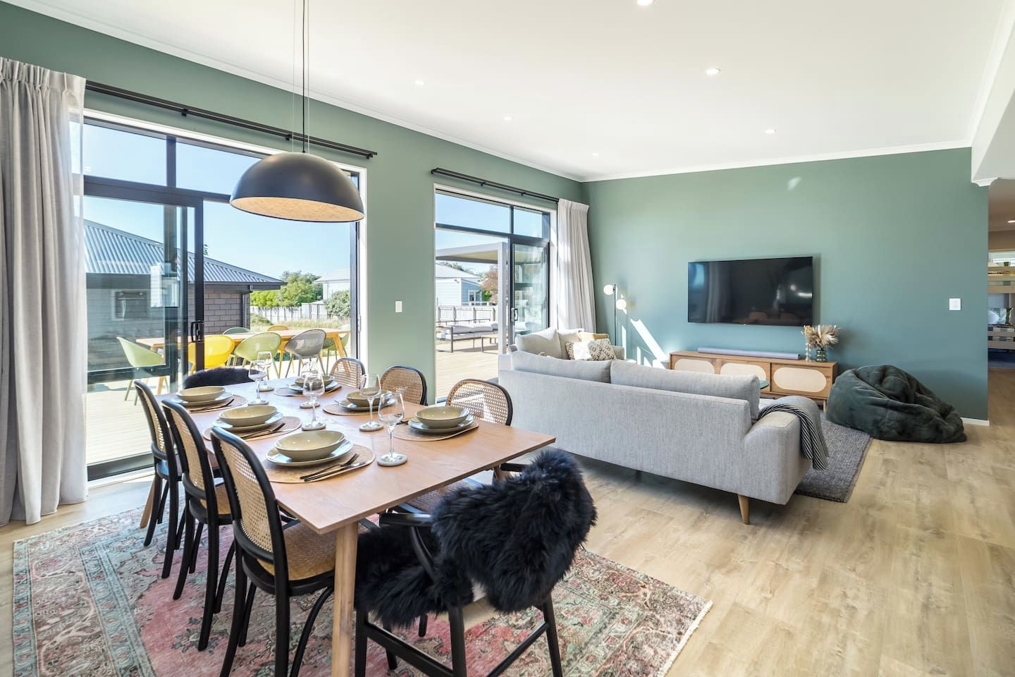 A modern living room with a sofa, television, and dining area with chairs and a table set for a meal.