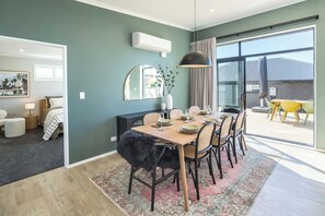 A modern dining area with a large table set for six, a black furry chair, and a view of the outdoors through a large window. - Sunset On Syrah, Martinborough (Martinborough)