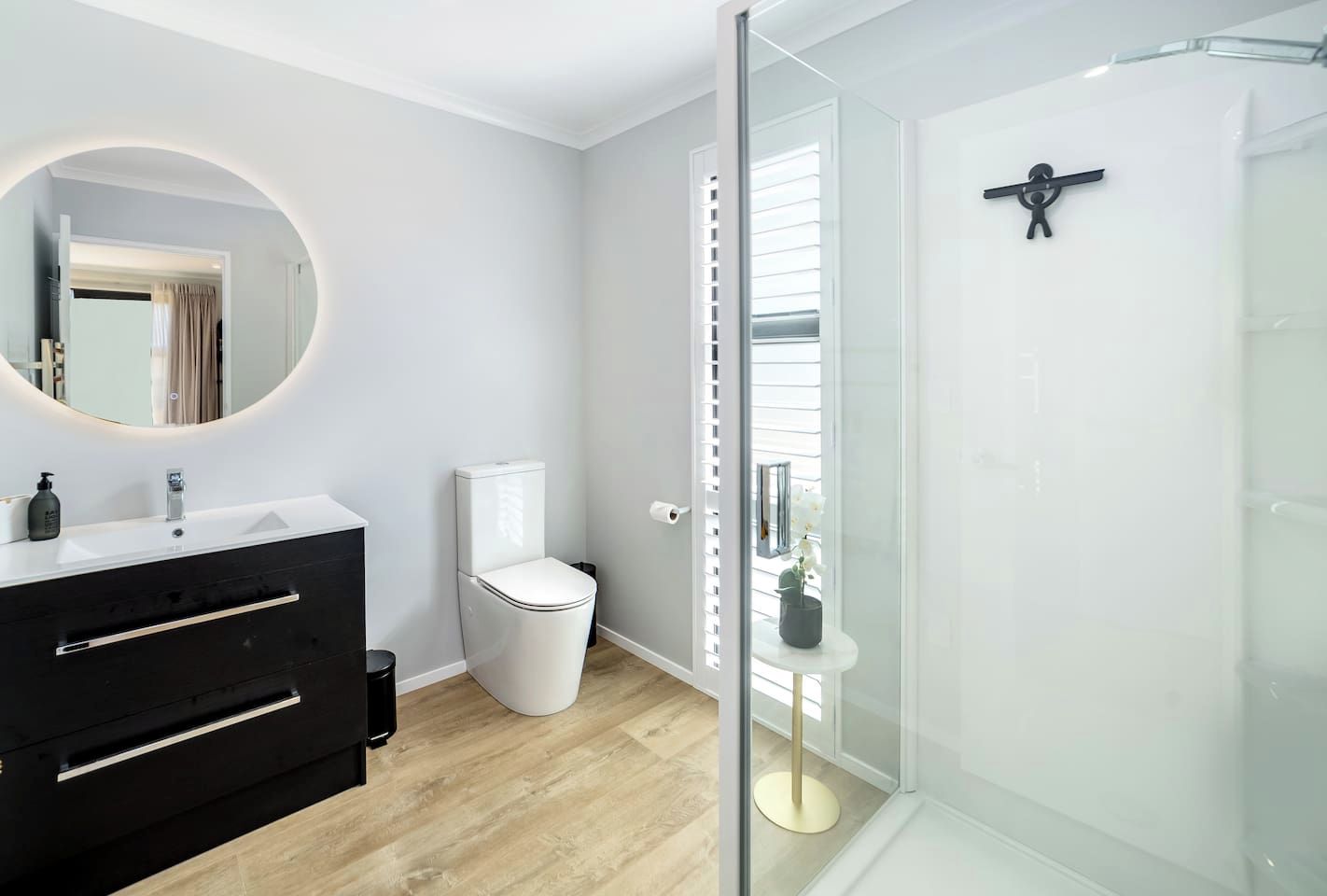 Ein modernes Badezimmer mit Duschkabine aus Glas, einer weißen Toilette und einem schwarzen Waschtisch mit rundem Spiegel.