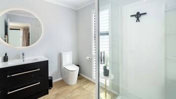 Ein modernes Badezimmer mit Duschkabine aus Glas, einer weißen Toilette und einem schwarzen Waschtisch mit rundem Spiegel.