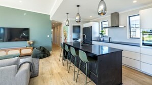 A modern kitchen with a central island, bar stools, pendant lighting, and a view of the adjacent living area. - Sunset On Syrah, Martinborough (Martinborough)