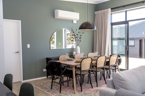 A dining area with a table set for six, surrounded by wicker chairs, a black furry chair, and a large pendant light. - Sunset On Syrah, Martinborough (Martinborough)