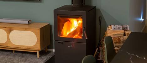 A wood-burning stove with visible flames, a wooden cabinet, and a dining table with chairs.