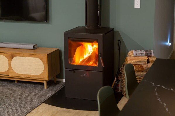 A wood-burning stove with visible flames, a wooden cabinet, and a dining table with chairs.