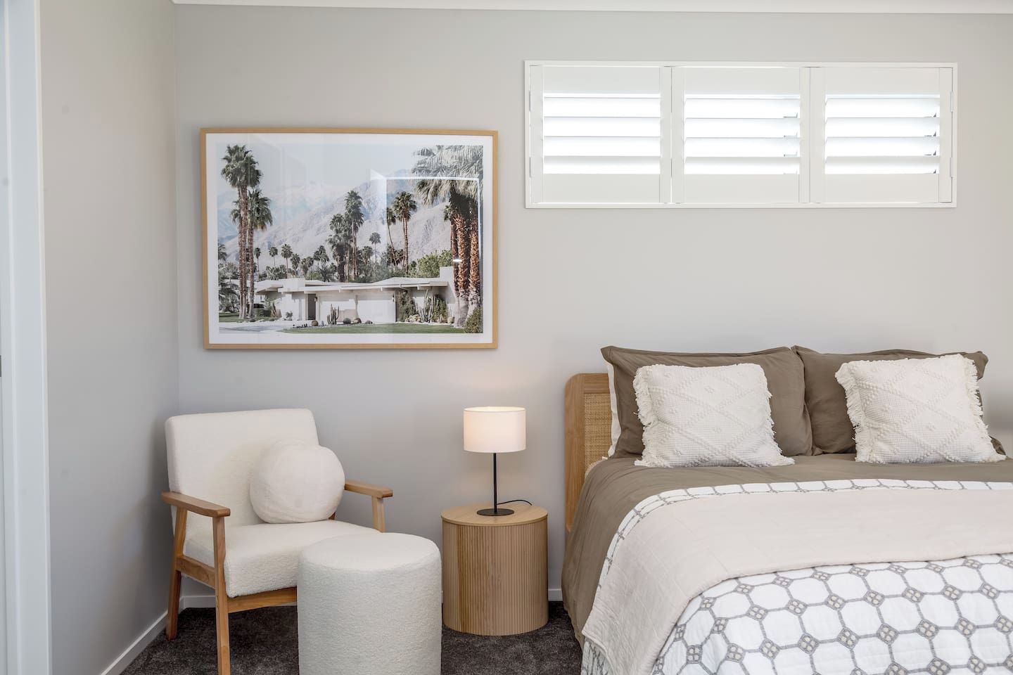Une chambre à coucher avec un lit, une chaise, une table de chevet, une lampe et un tableau encadré au mur.