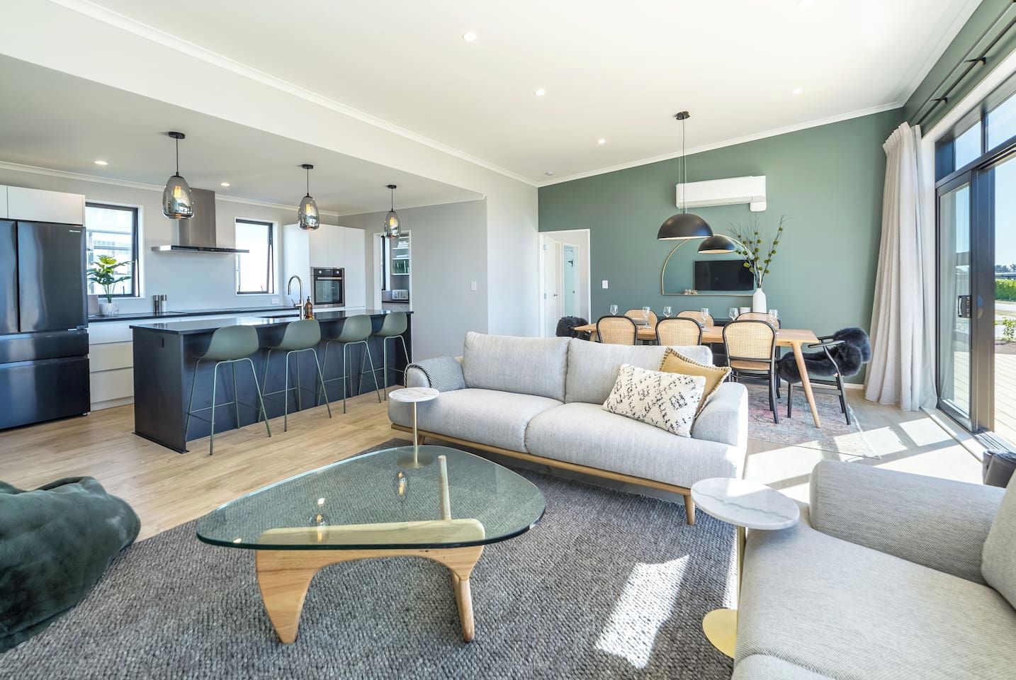 A modern kitchen with a central island, dining area with chairs, and a living room with a sofa and coffee table.