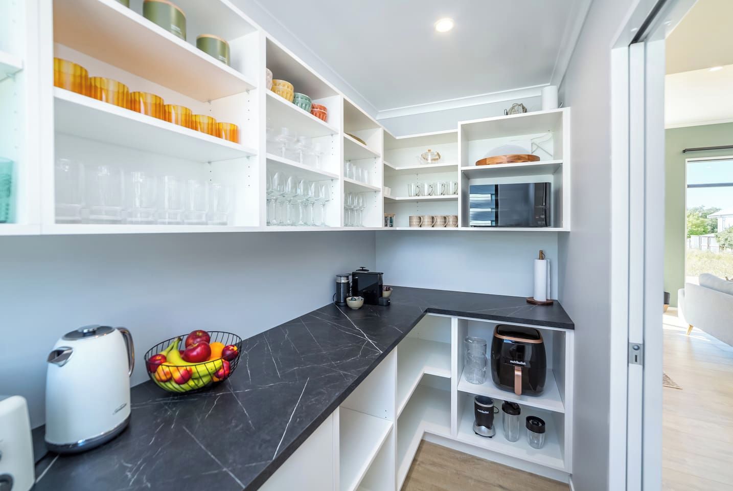 Une cuisine moderne avec des meubles blancs, un plan de travail noir et divers appareils de cuisine.