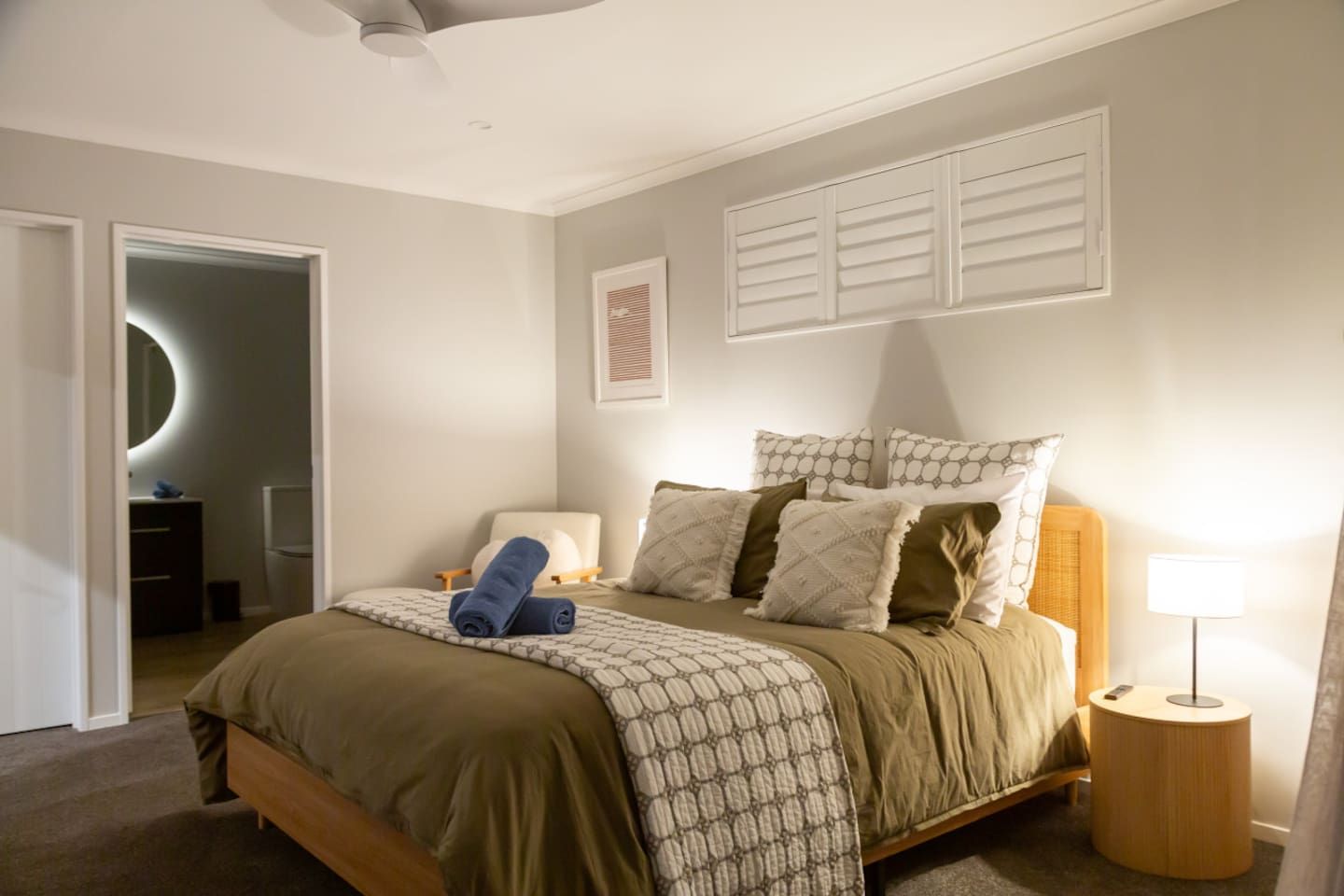 Een slaapkamer met een bed, een nachtkastje, een lamp, een spiegel en een deur die naar een andere kamer leidt.
