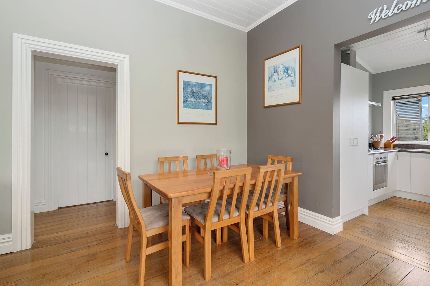 A dining area with a wooden table and chairs, a white door, and two framed pictures on the wall.
