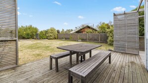 Une terrasse en bois avec une table de pique-nique et des bancs, entourée d’une clôture en bois et d’arbres.
