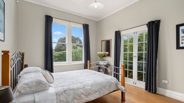 A bedroom with a bed, a nightstand, a dresser, a window with curtains, and a view of greenery outside. - Applecross Cottage | Cozy Stay, Walk to Martinborough Square (Martinborough)