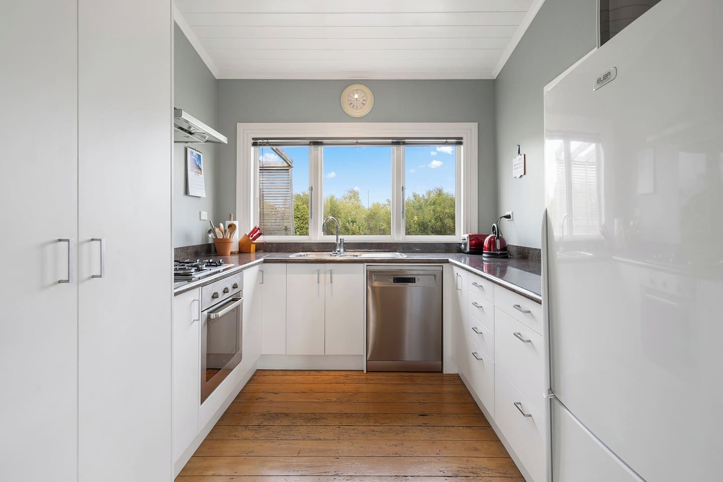 A modern kitchen with white cabinets, stainless steel appliances, and a wooden floor.