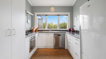A modern kitchen with white cabinets, stainless steel appliances, and a wooden floor.