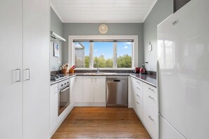 A modern kitchen with white cabinets, stainless steel appliances, and a wooden floor. - Applecross Cottage, Martinborough (Martinborough)