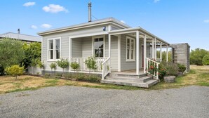 A single-story house with a covered porch, a chimney, and a small garden with potted plants. - Applecross Cottage | Cozy Stay, Walk to Martinborough Square (Martinborough)