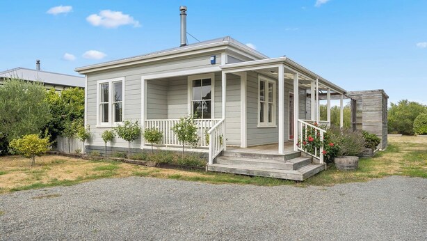 Une maison de plain-pied avec un porche, une cheminée et un petit jardin.