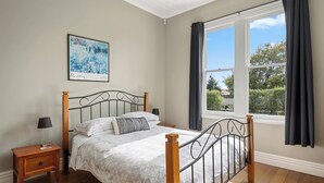 Une chambre à coucher avec un lit, une table de chevet, une fenêtre avec des rideaux et un tableau au mur.