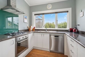 Une cuisine moderne équipée d’une cuisinière à gaz, d’un four, d’un lave-vaisselle et d’une fenêtre donnant sur les arbres.