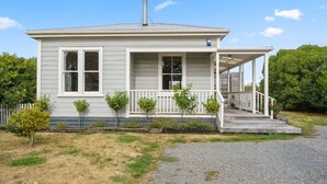A single-story house with a porch, a chimney, and a small garden area with young trees. - Applecross Cottage | Cozy Stay, Walk to Martinborough Square (Martinborough)