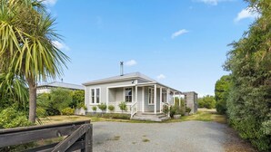 Une maison de plain-pied avec un porche, entourée de verdure et dotée d’une allée en gravier.