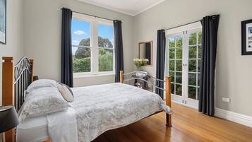 Quarto com cama, mesa de cabeceira, espelho e janela com cortinas.