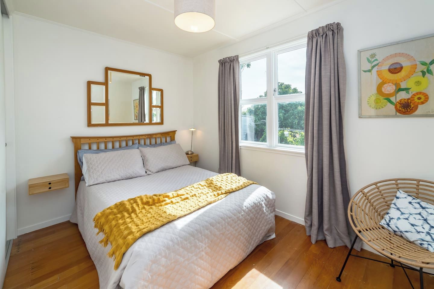 A bedroom with a bed, a bedside table, a chair, a window with curtains, and a painting on the wall.