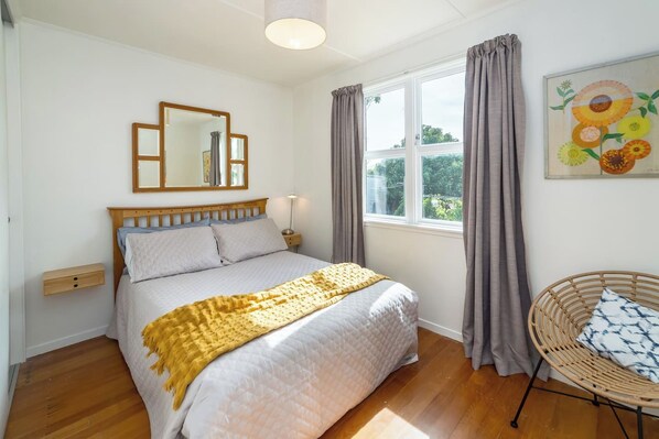 A bedroom with a bed, a bedside table, a chair, a window with curtains, and a painting on the wall.