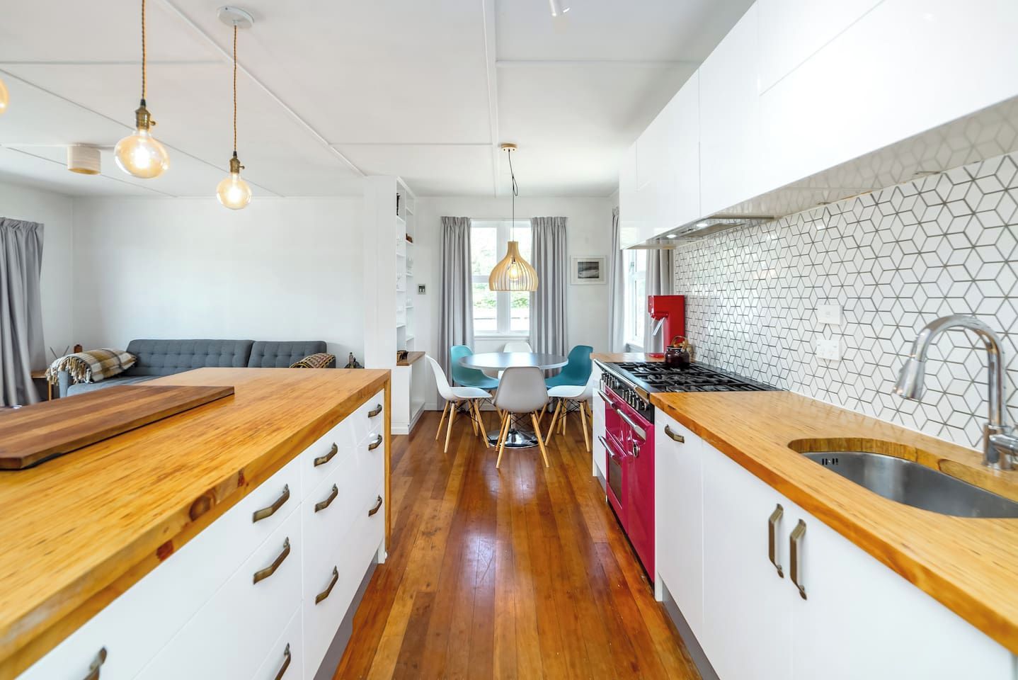 A modern kitchen with a wooden island, a dining area with chairs, and a red stove.