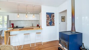 Cocina moderna con una isla central, taburetes de bar, iluminación colgante, un horno a leña azul y un salpicadero de azulejos.